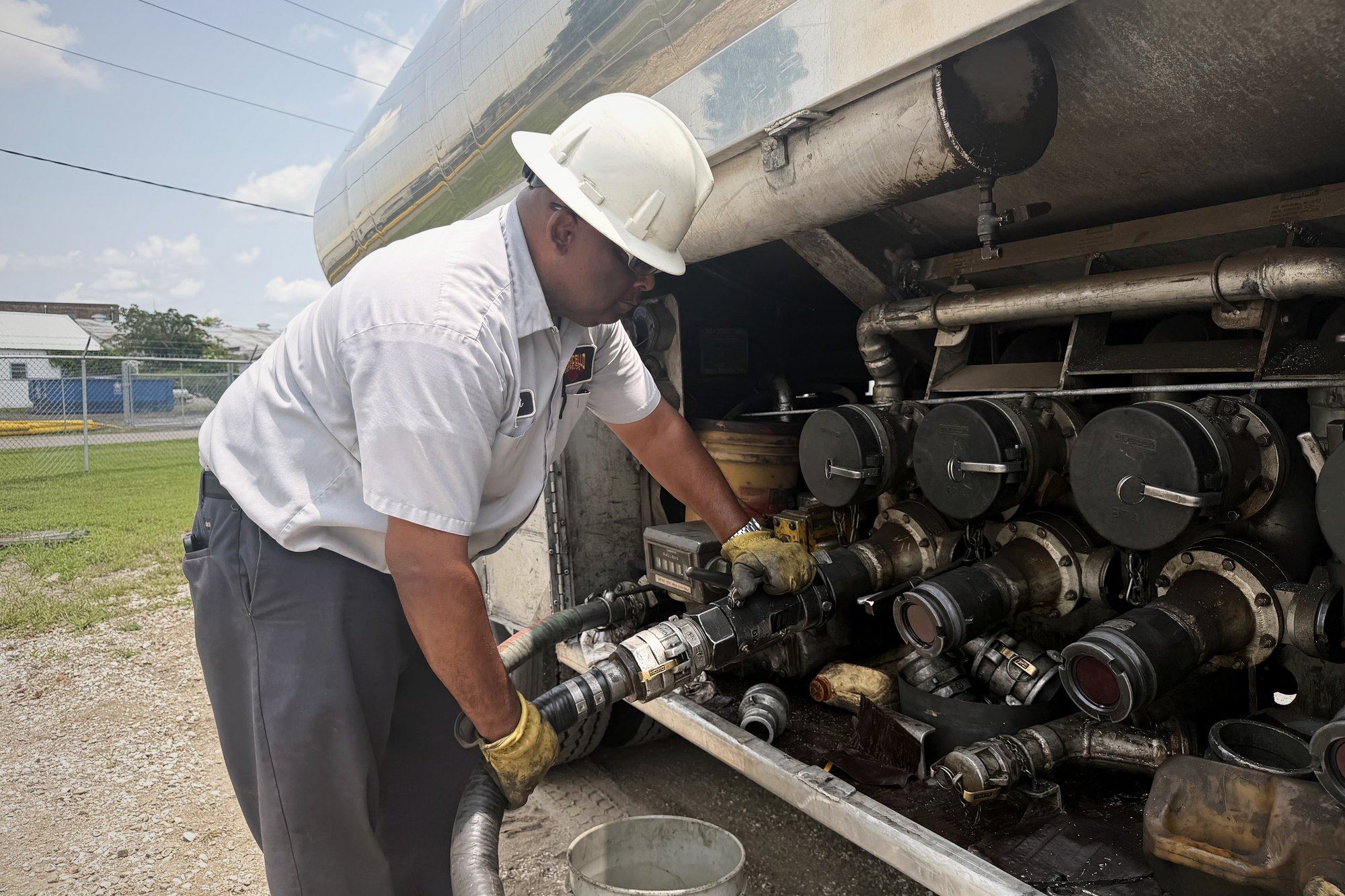 Driver connecting a hose to a tanker manifold at an industrial site